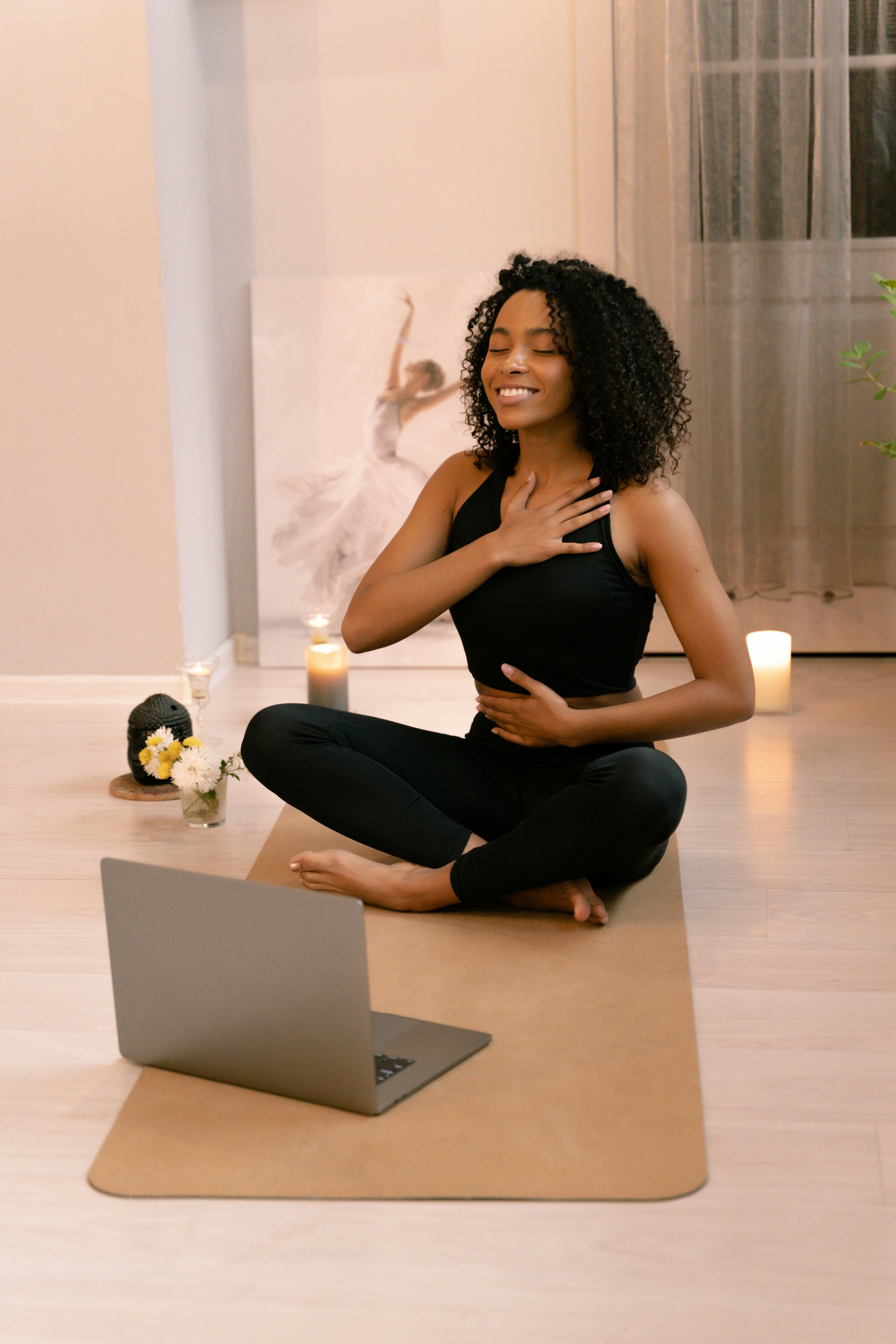 An African American woman doing breathing exercises happily on her yoga mat.